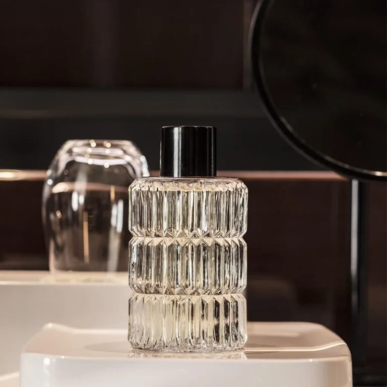 Flacon d'Eau de Cologne Les Bains Guerbois posé sur le rebord d'un lavabo blanc, fond sombre